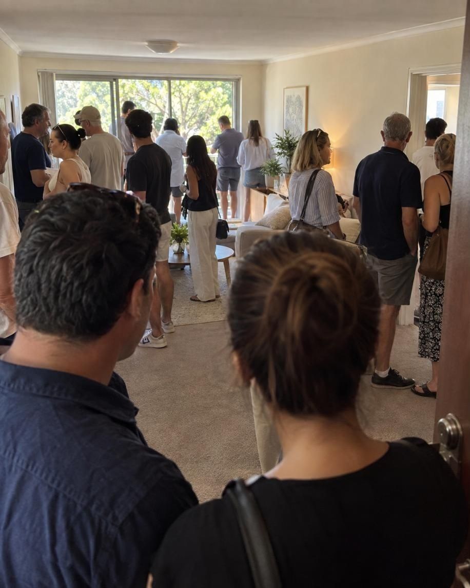 A packed home open: a living room full of buyers, seen from the front door