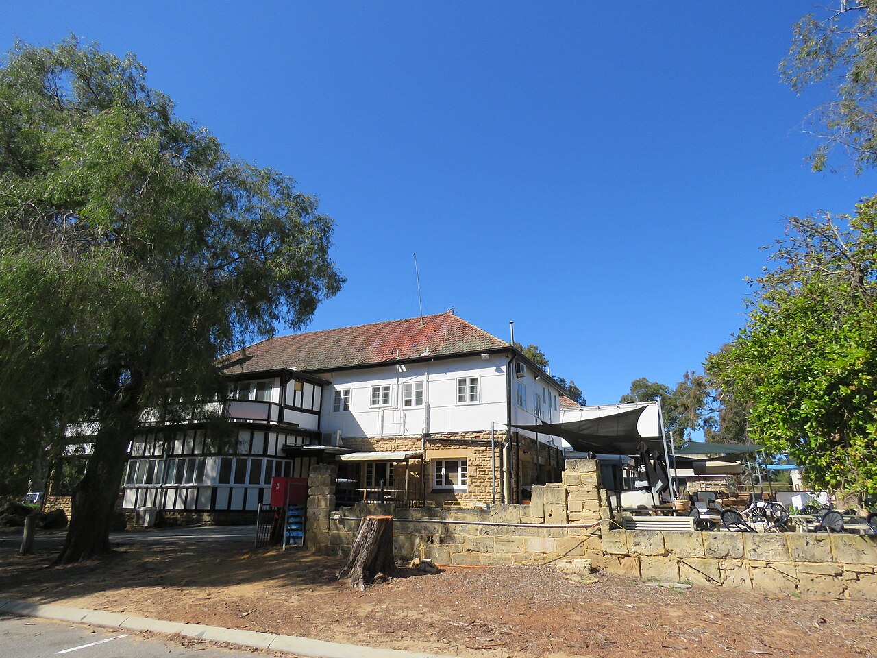 The two-storey, half-timbered Yanchep Inn seen from the road, with a stone wall in front and trees either side.