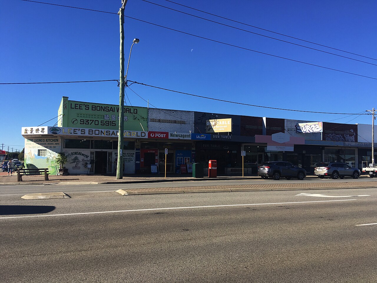 A row of single-storey shops with signs above their awnings, facing Grand Promenade in Bedford.